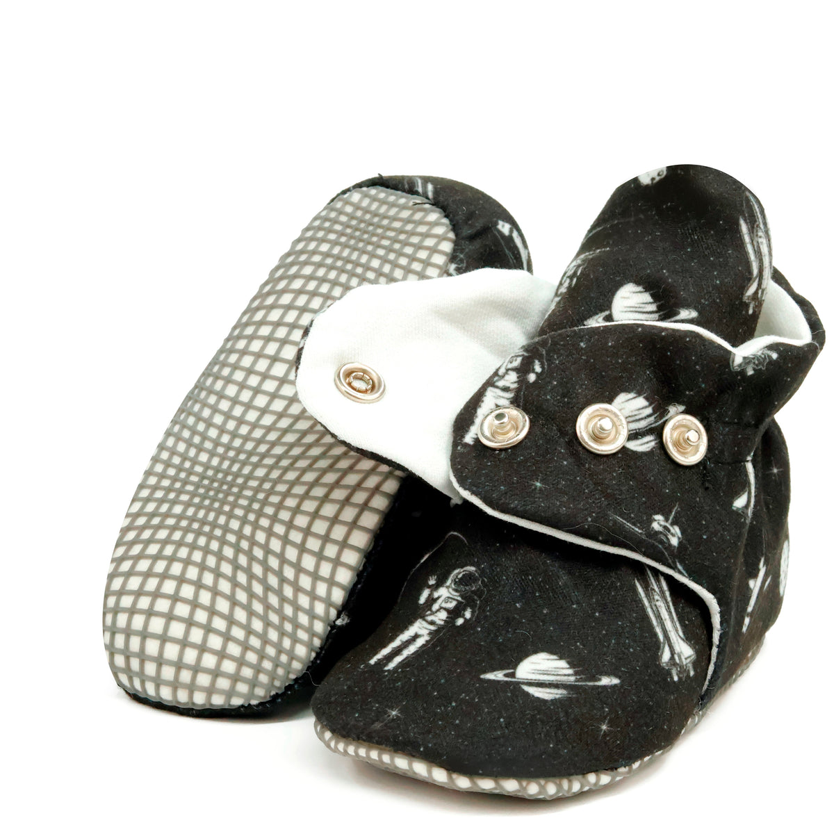 Black baby booties with white space motifs and snap straps, showing one sole and an open snap strap on white.