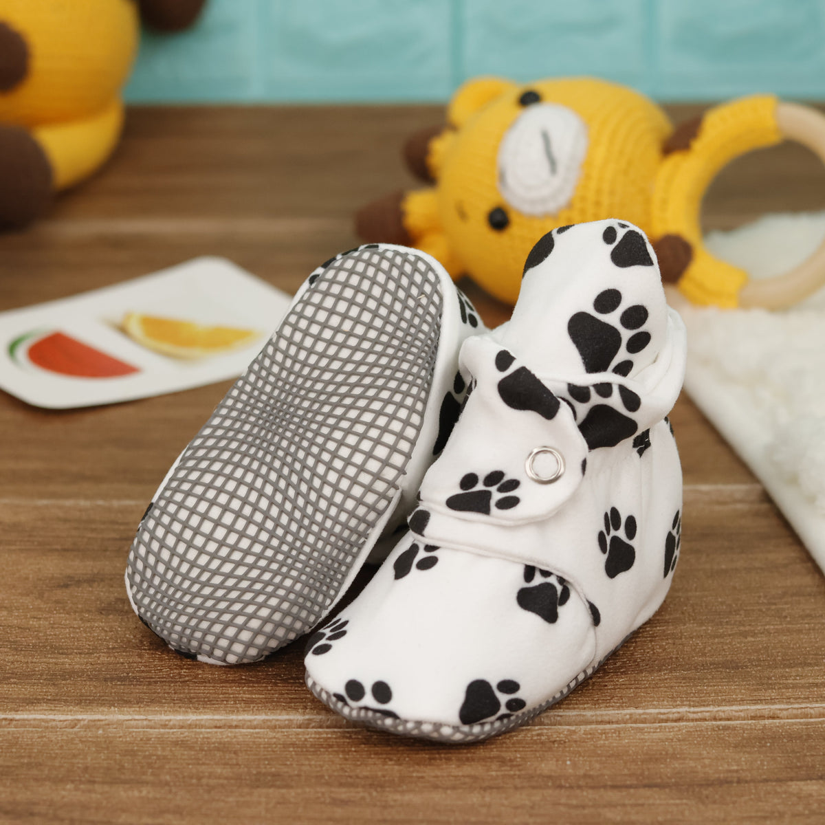 White baby booties with black paw prints and snap straps arranged on a surface with one sole facing the camera.