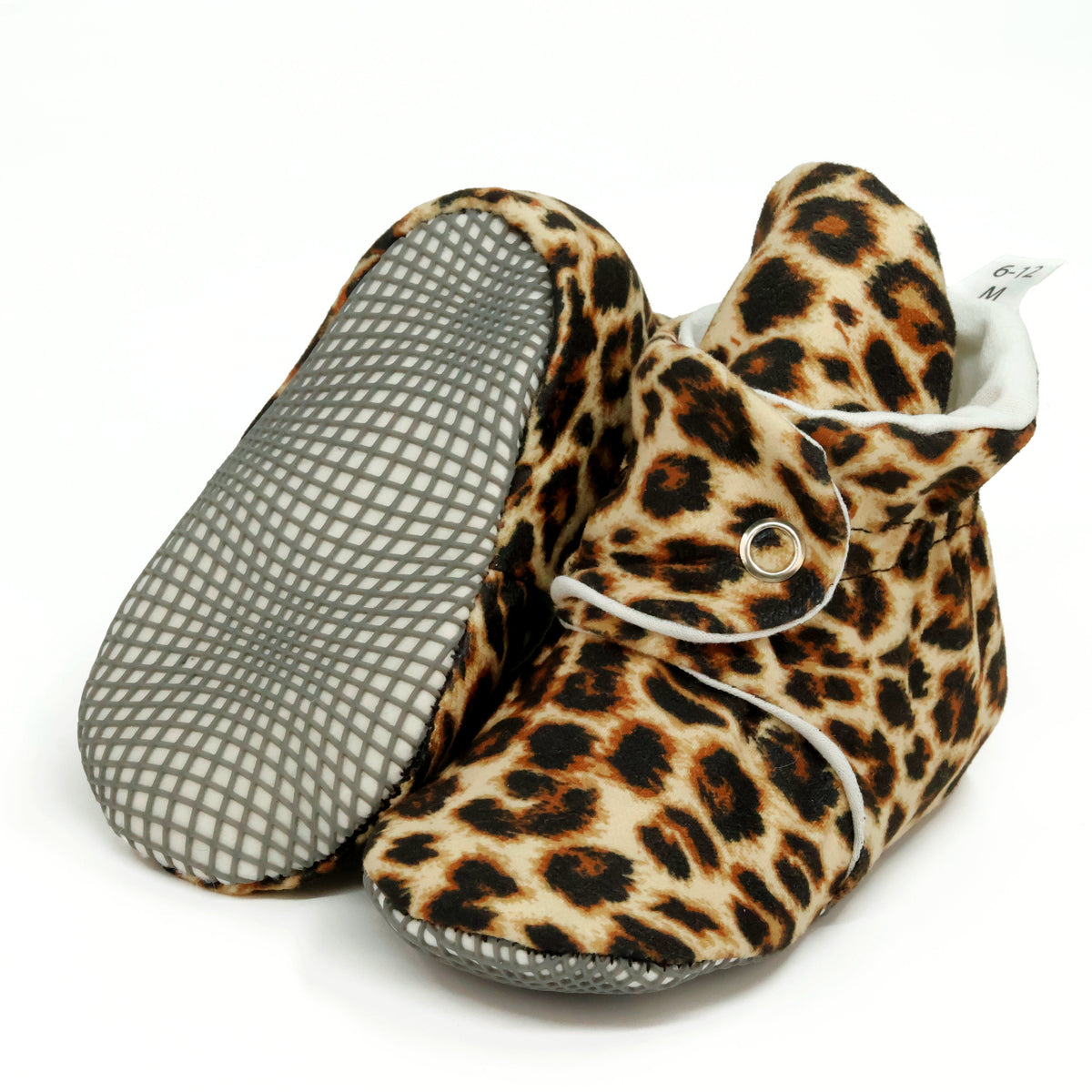 Tan baby booties with brown-and-black leopard spots and snap straps, with one sole facing the camera on a white background.