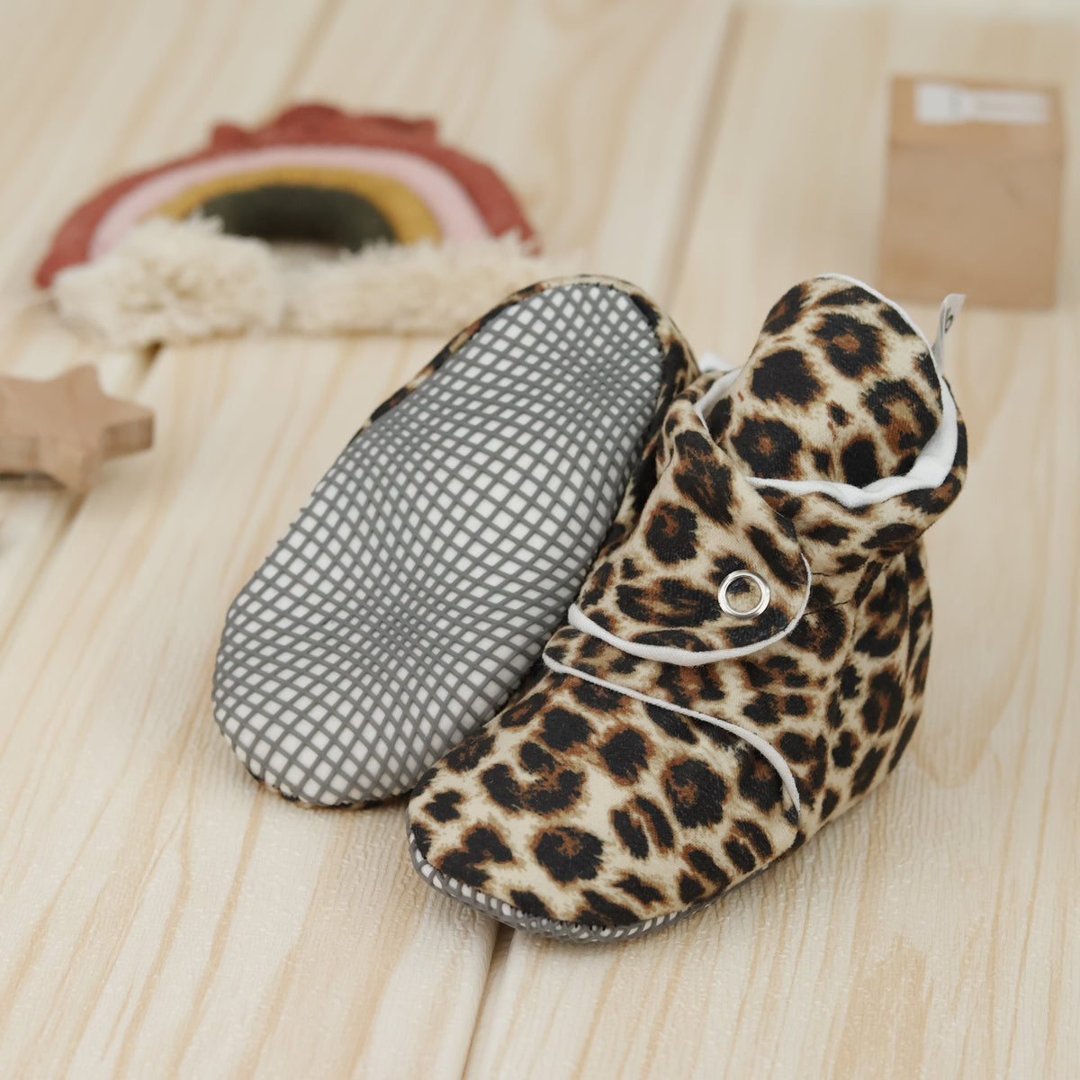 Tan baby booties with brown-and-black leopard spots and snap straps arranged on a surface with one sole facing the camera.
