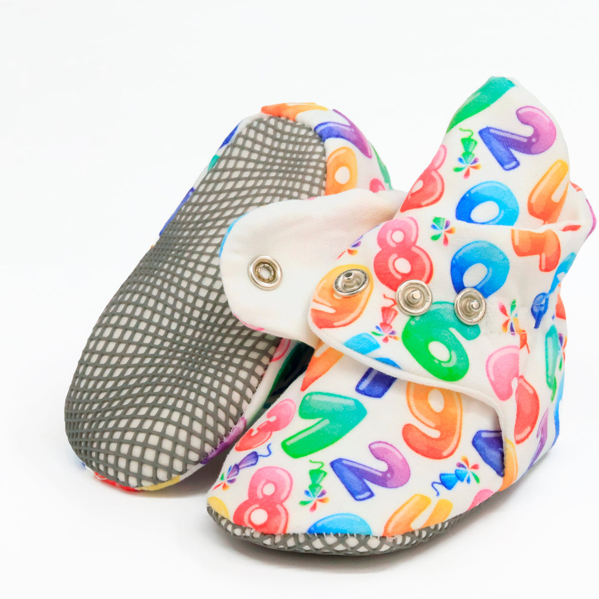 White baby booties with colorful numbers and snap straps, showing one sole and an open snap strap on white.