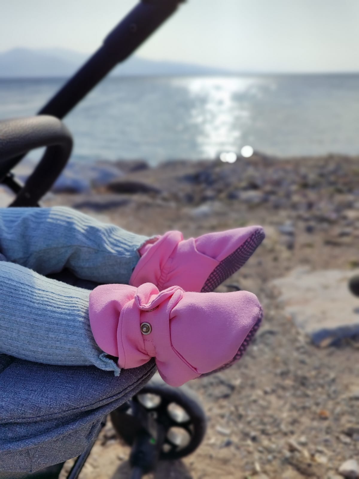 Pink booties worn in a stroller beside the sea, front view.