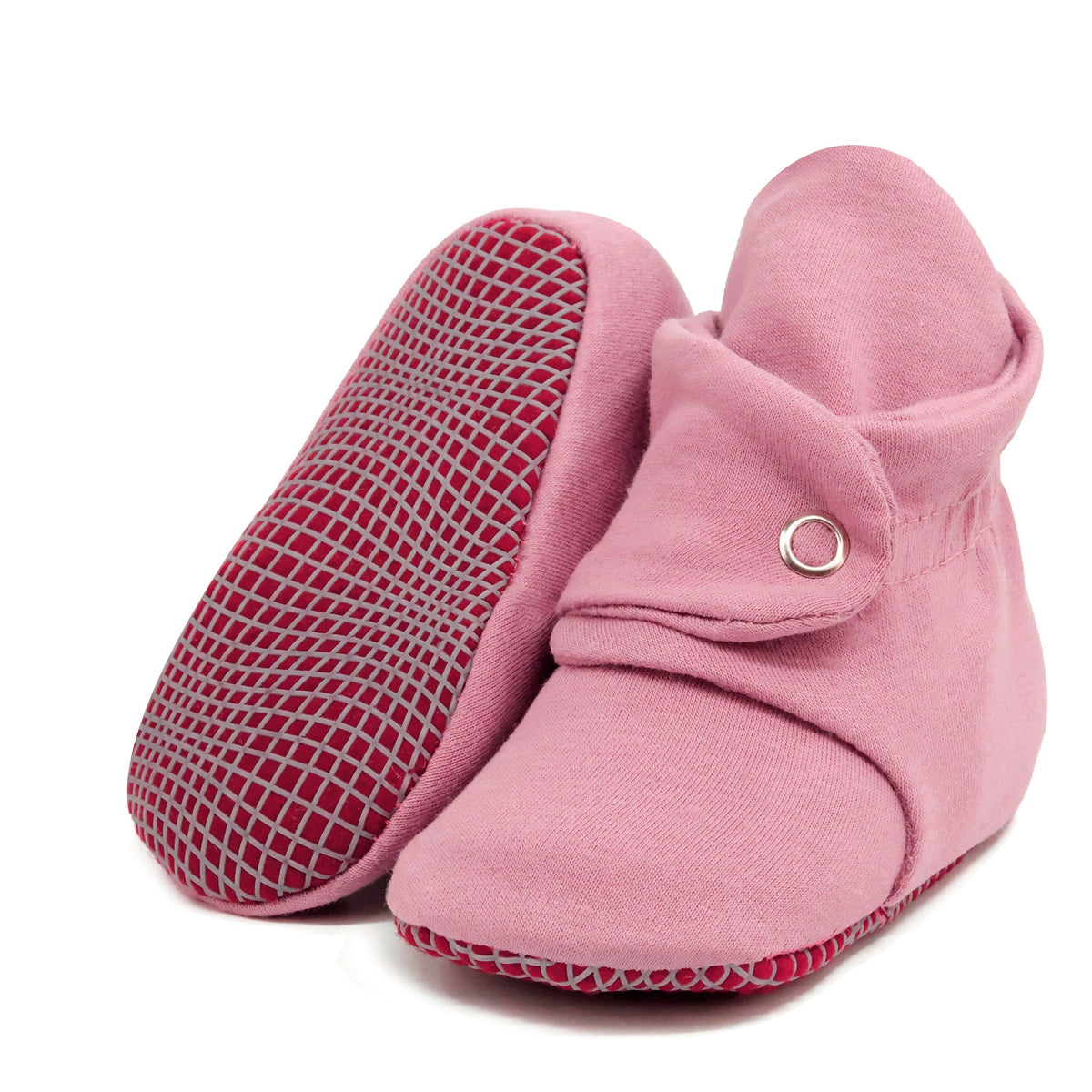 Dusty rose fabric baby booties with snap straps and gray grip soles, with one sole facing the camera on a white background.
