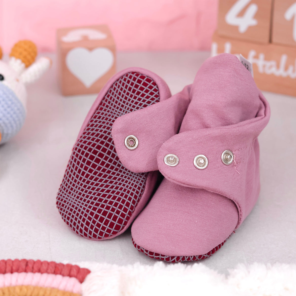 Close-up of dusty rose fabric baby booties with snap straps and gray grip soles, showing one sole and an open snap strap.