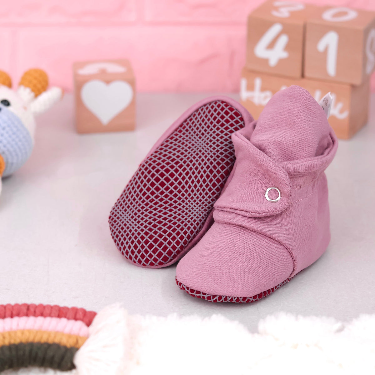 Dusty rose fabric baby booties with snap straps and gray grip soles arranged on a surface with one sole facing the camera.