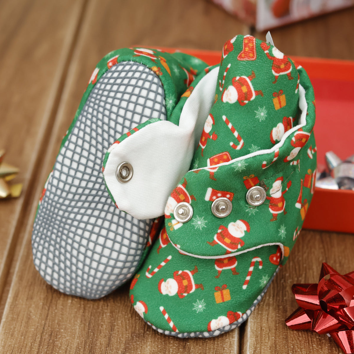 Close-up of green baby booties with Santa Claus Christmas print and snap straps, showing one sole and an open snap strap.