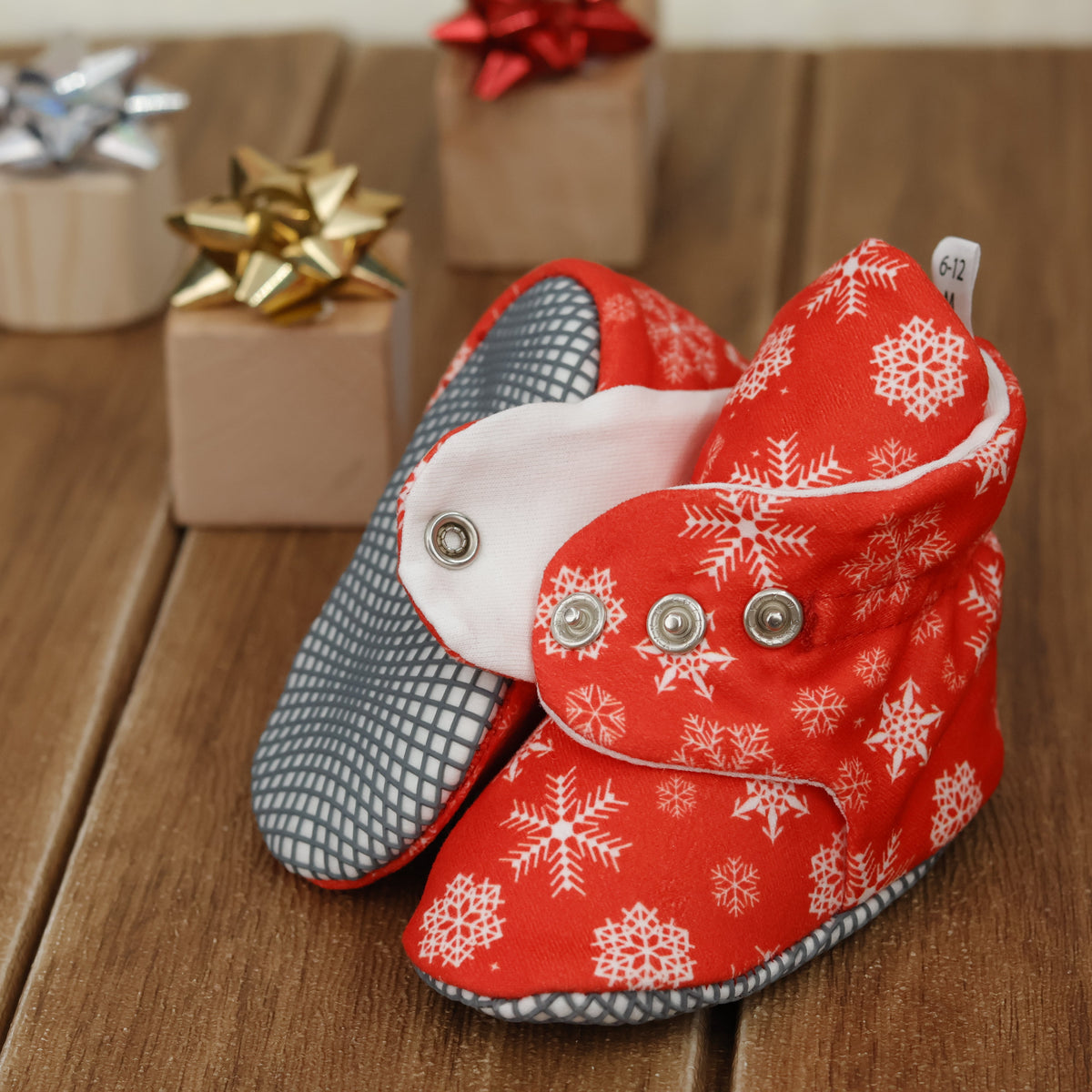 Close-up of red baby booties with white snowflakes and snap straps, showing one sole and an open snap strap.