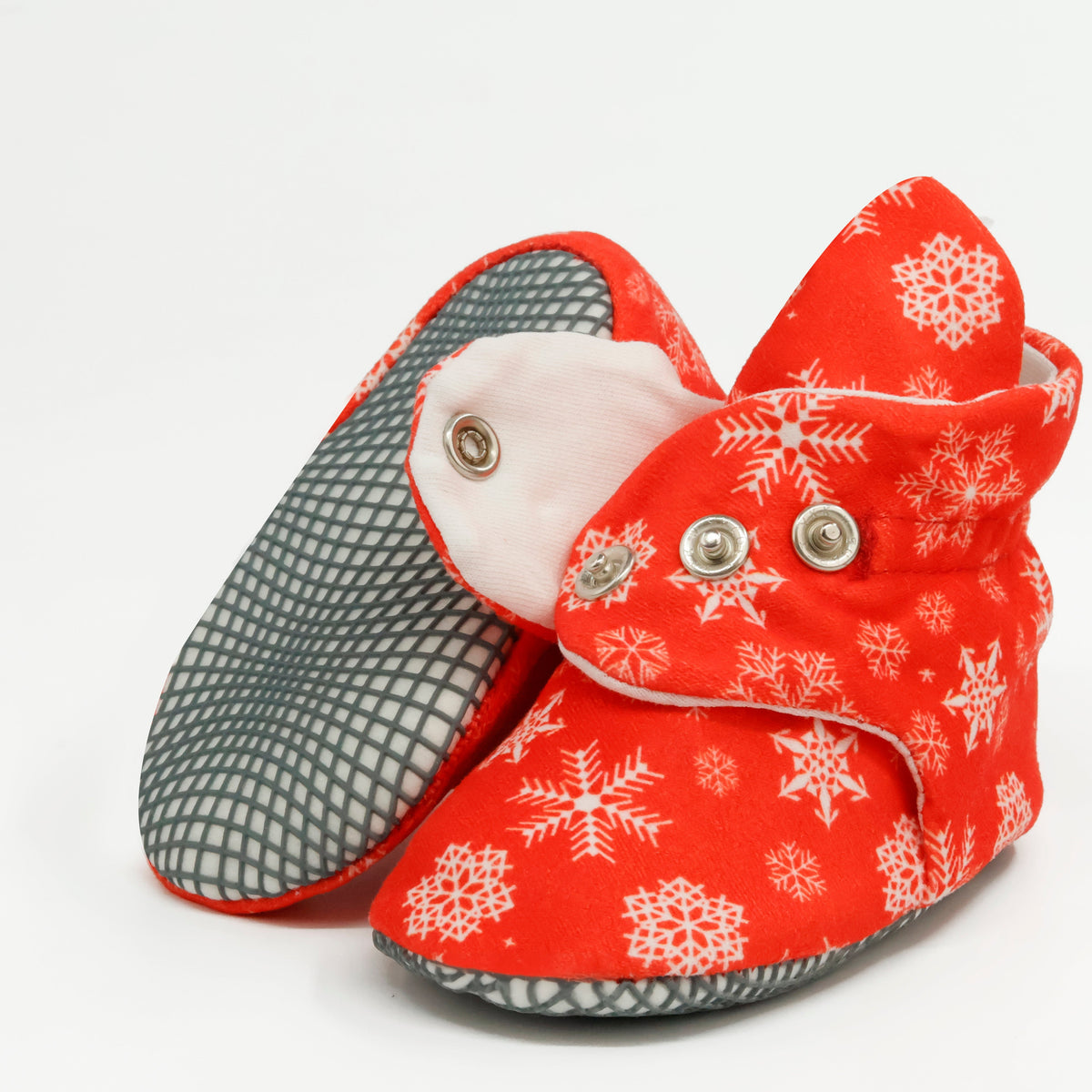 Red baby booties with white snowflakes and snap straps, showing one sole and an open snap strap on white.