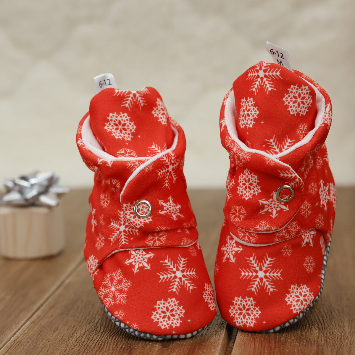 Front view of a pair of red baby booties with white snowflakes and snap straps.