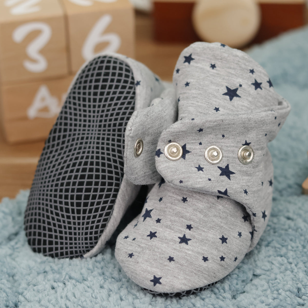 Close-up of light gray baby booties with dark stars and snap straps, showing one sole and an open snap strap.