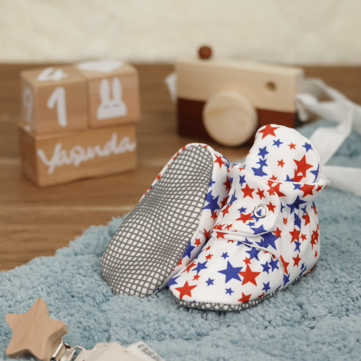 White baby booties with red-and-blue stars and snap straps arranged on a surface with one sole facing the camera.