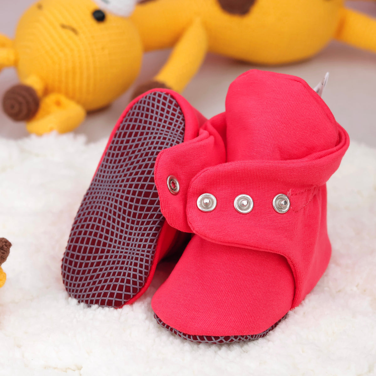 Close-up of bright red fabric baby booties with snap straps and gray grip soles, showing one sole and an open snap strap.
