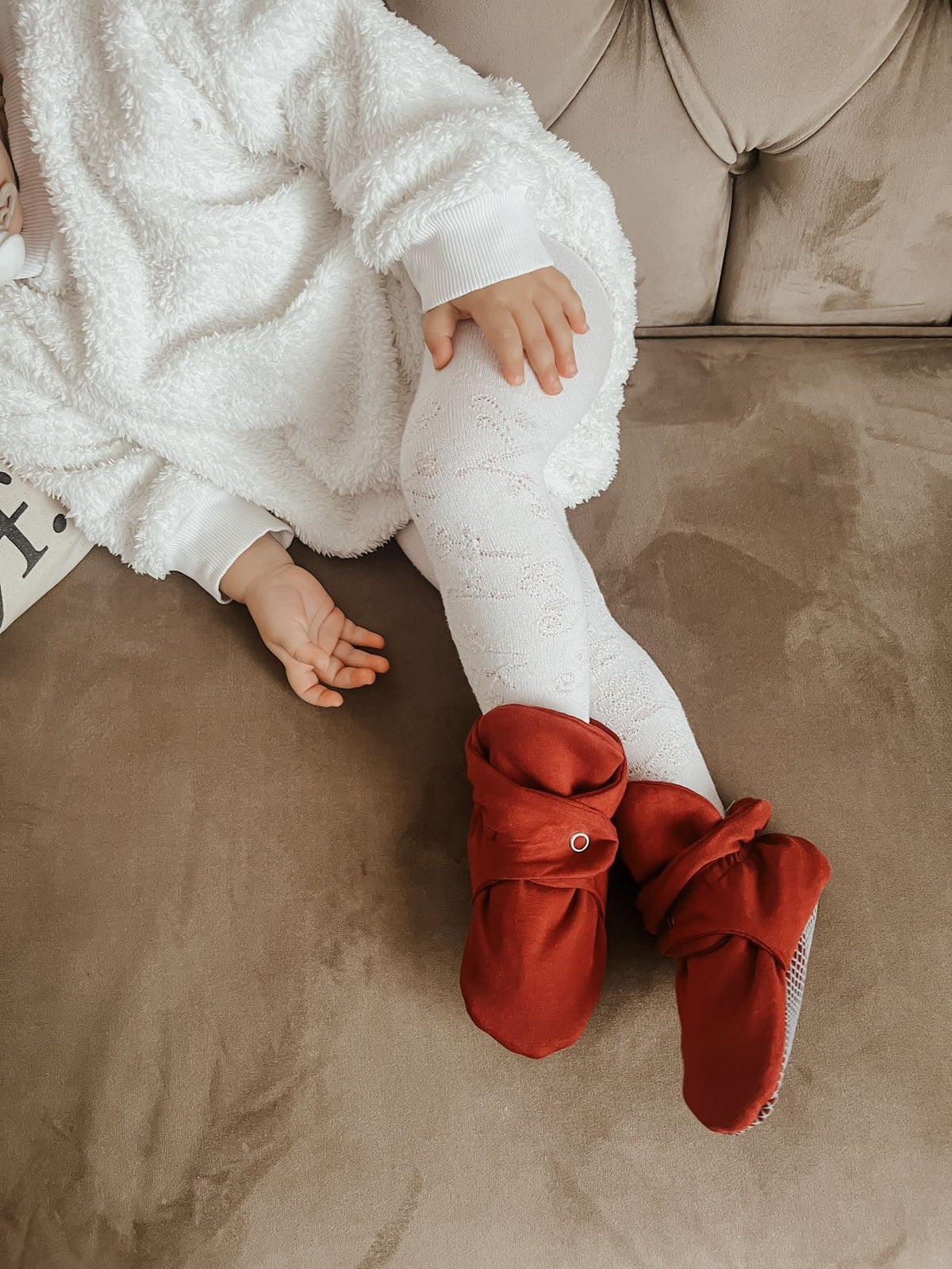 Child seated on a sofa wearing red booties.