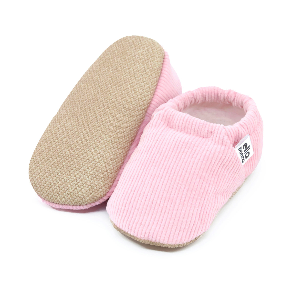 Pink ribbed corduroy slip-on baby moccasins with tan soles, with one sole facing the camera on a white background.
