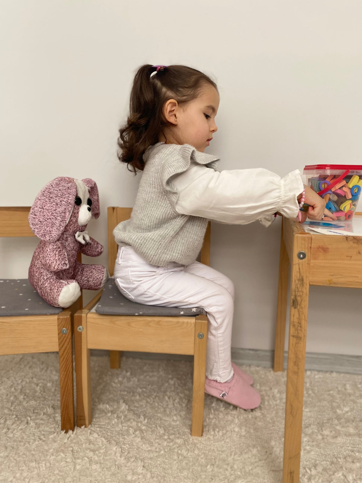 Side view of a child seated at a table wearing pink corduroy moccasins.