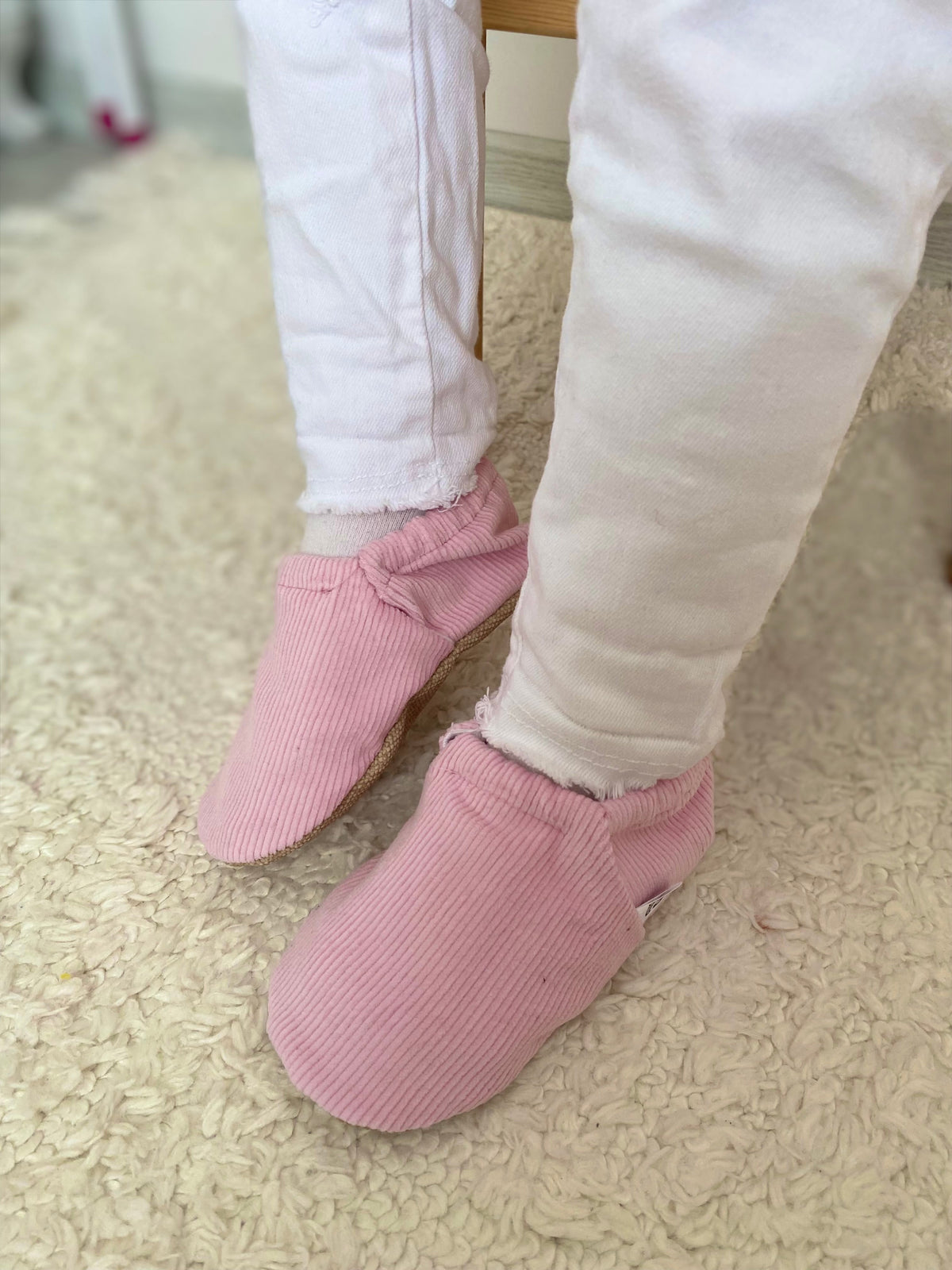 Front close-up of pink corduroy moccasins worn with pale trousers.