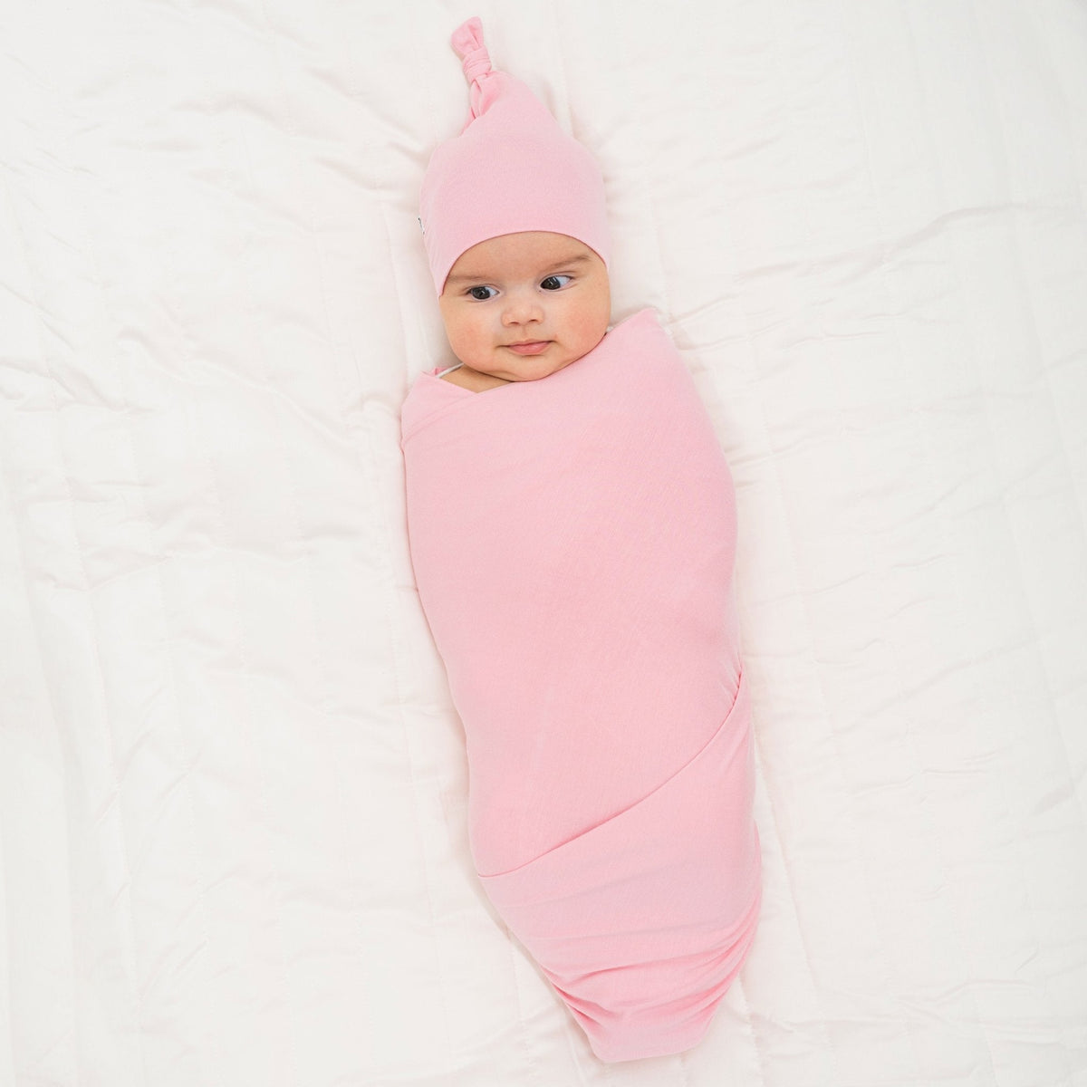 Baby wrapped in Bam & Stitch Pink Blossom Swaddle with a coordinating knotted hat.