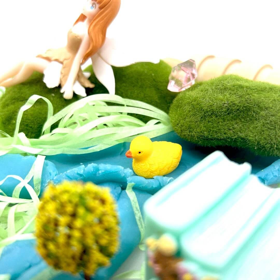 Yellow duck figure on blue playdough below the Pixie Hollow fairy