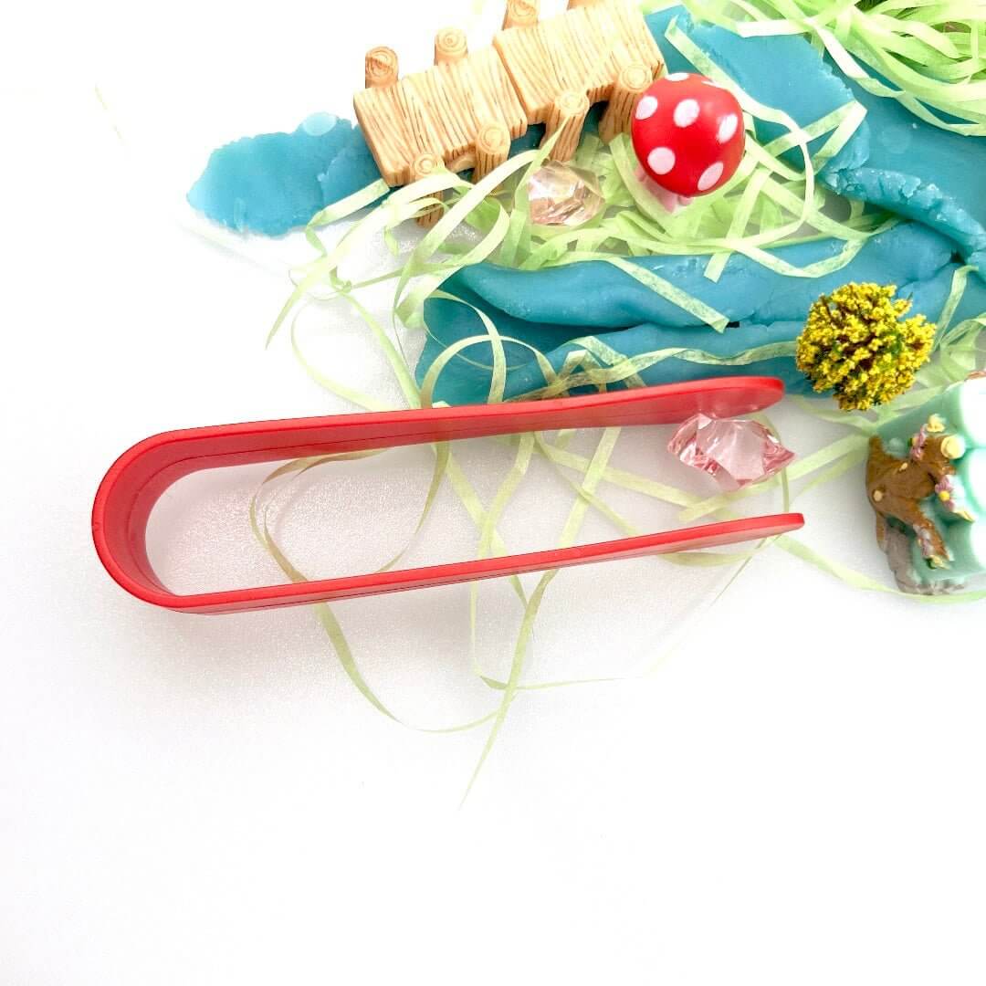 Overhead view of red tongs and a pink gem beside the fairy playdough scene