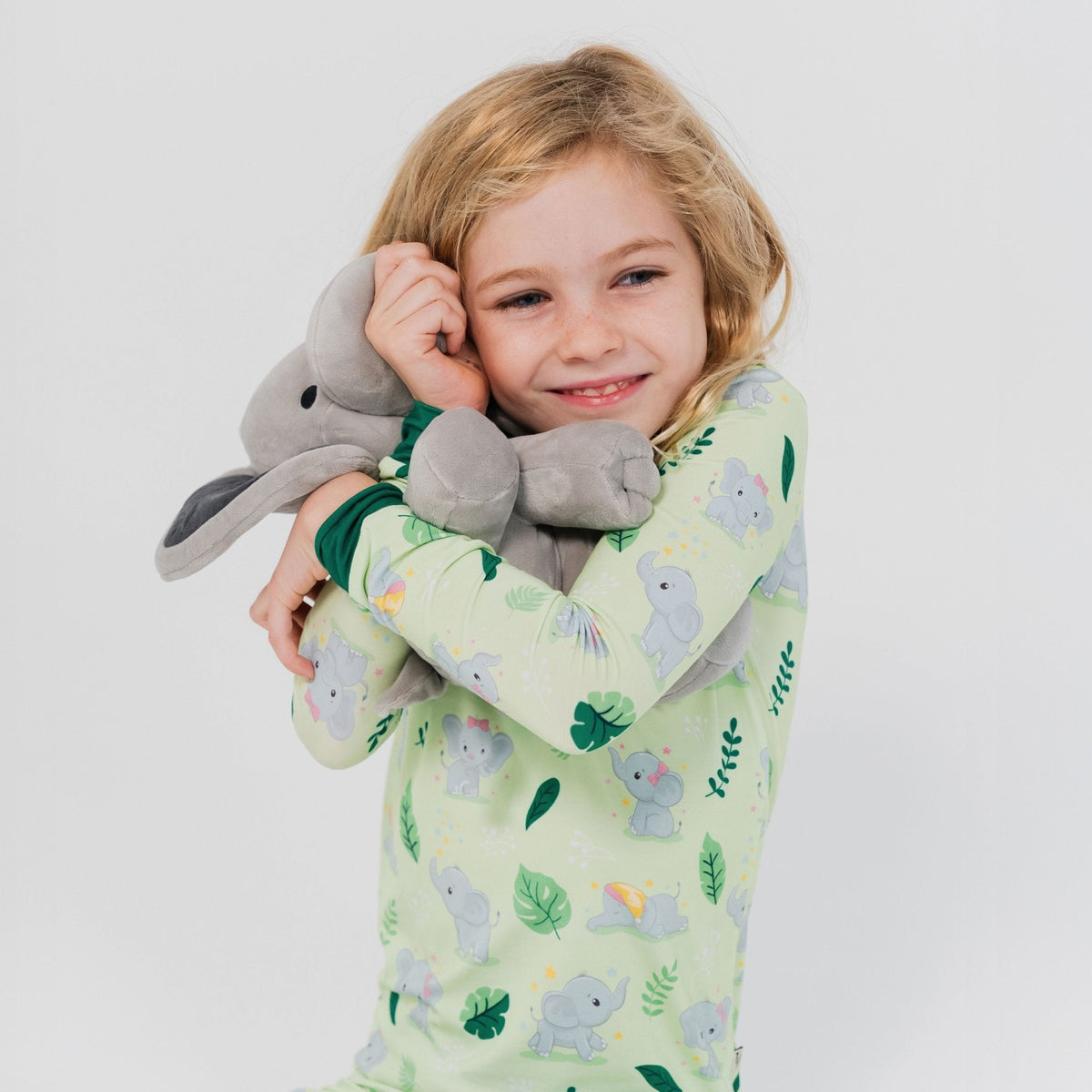 Child leaning against a plush elephant while wearing Bam & Stitch Playfully Strong Long Sleeve Pajamas.
