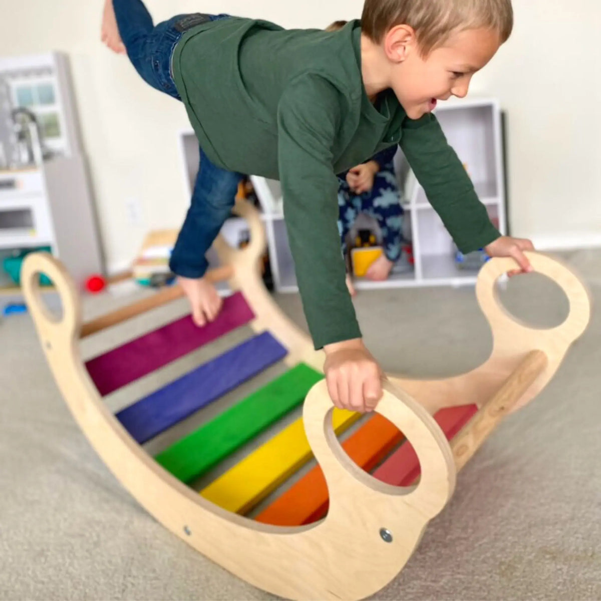 Child balancing on a rainbow-slat rocker while holding its circular handles.