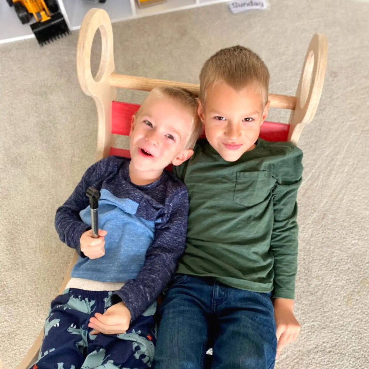 Two children reclining together in a rainbow-slat rocker.