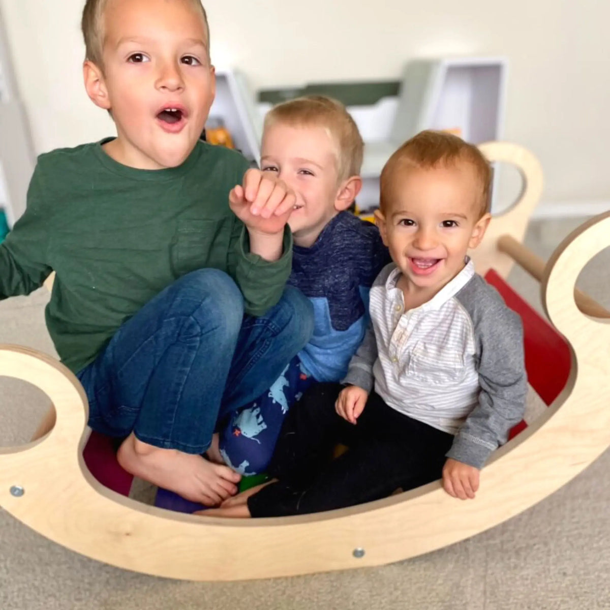 Three children sitting together in a rainbow-slat rocker.