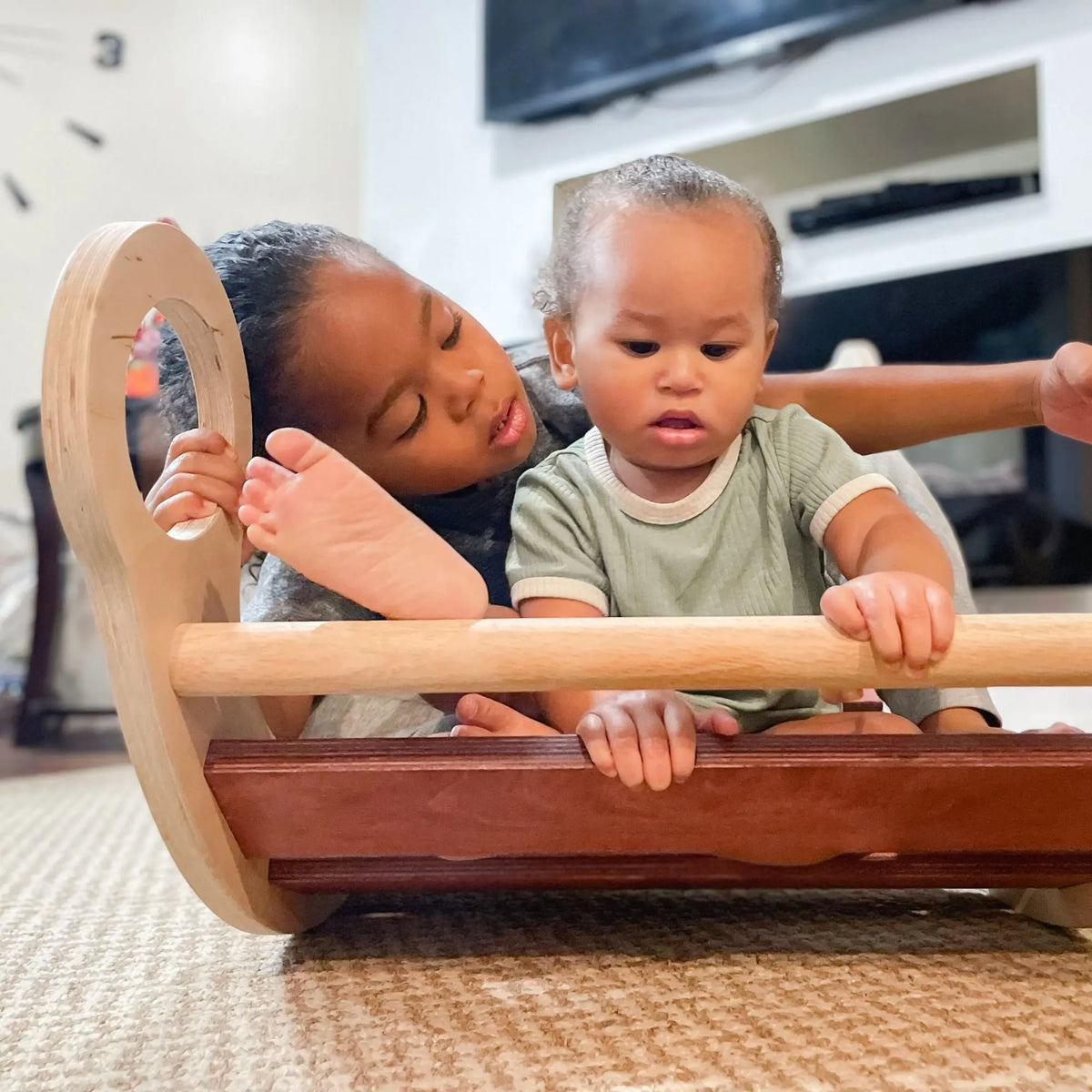 Two children seated together in a reddish-brown-slat rocker, viewed from the front.