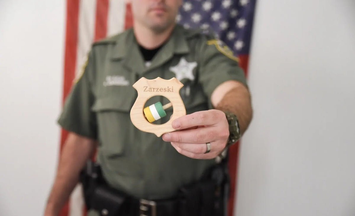 Adult holding a wooden shield rattle in front of a uniform
