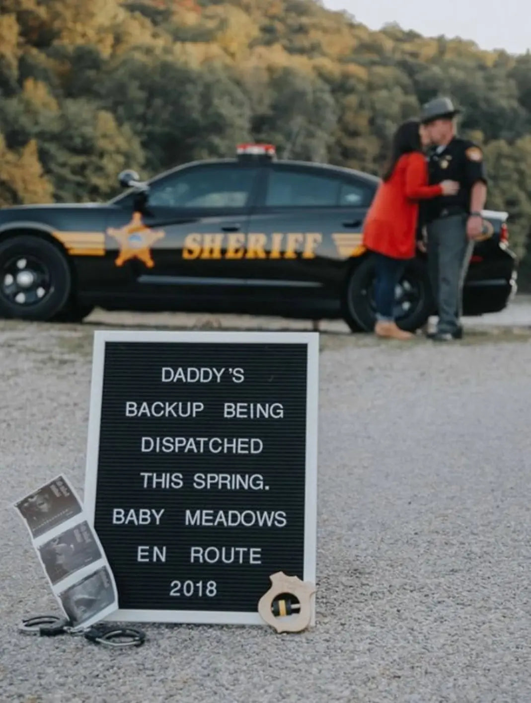 Birth-announcement display with a shield rattle in front of an emergency-services vehicle