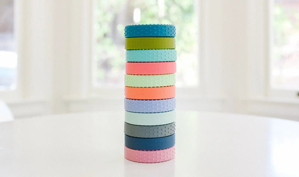 A tower of silicone-wrapped wooden teething rings showing available photo color examples