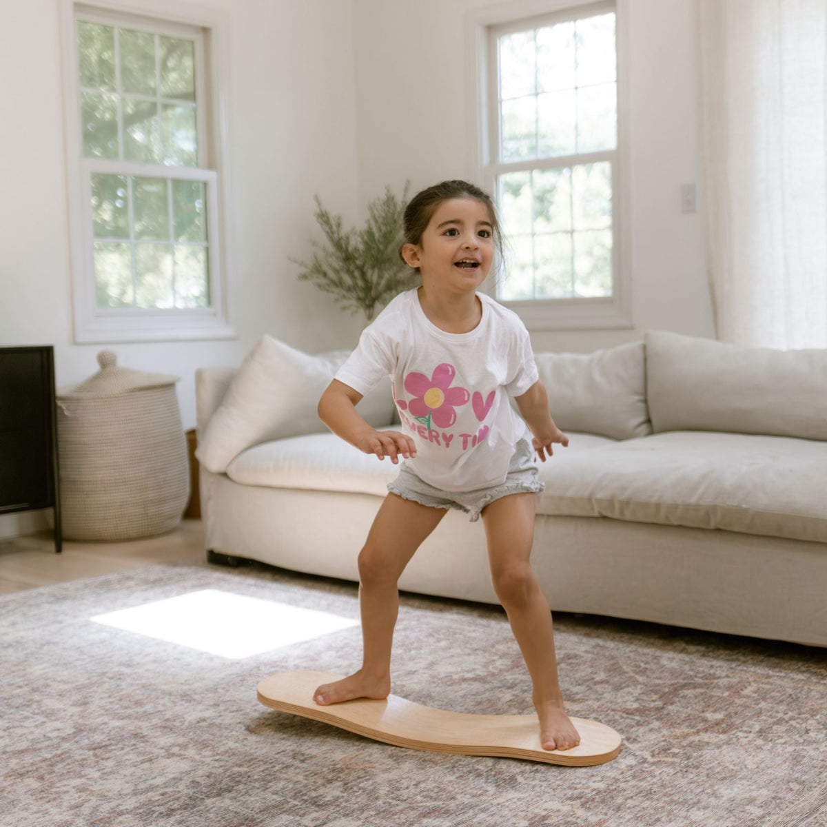 Child balancing with bent knees on a pale Spinzee board in front of a sofa.