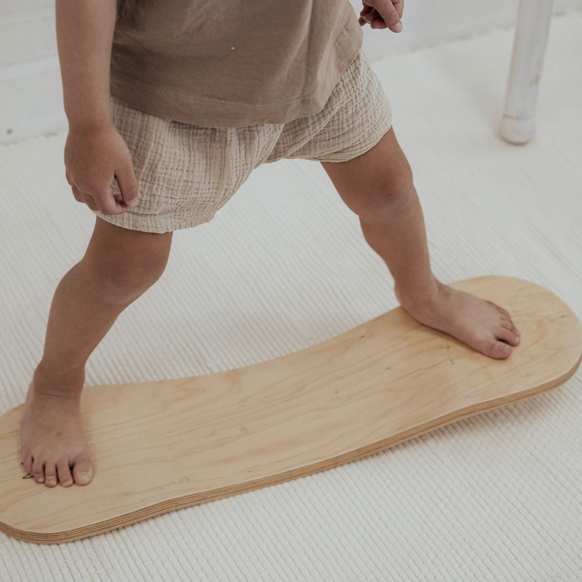 Close-up of a child standing barefoot near both ends of a pale Spinzee board.