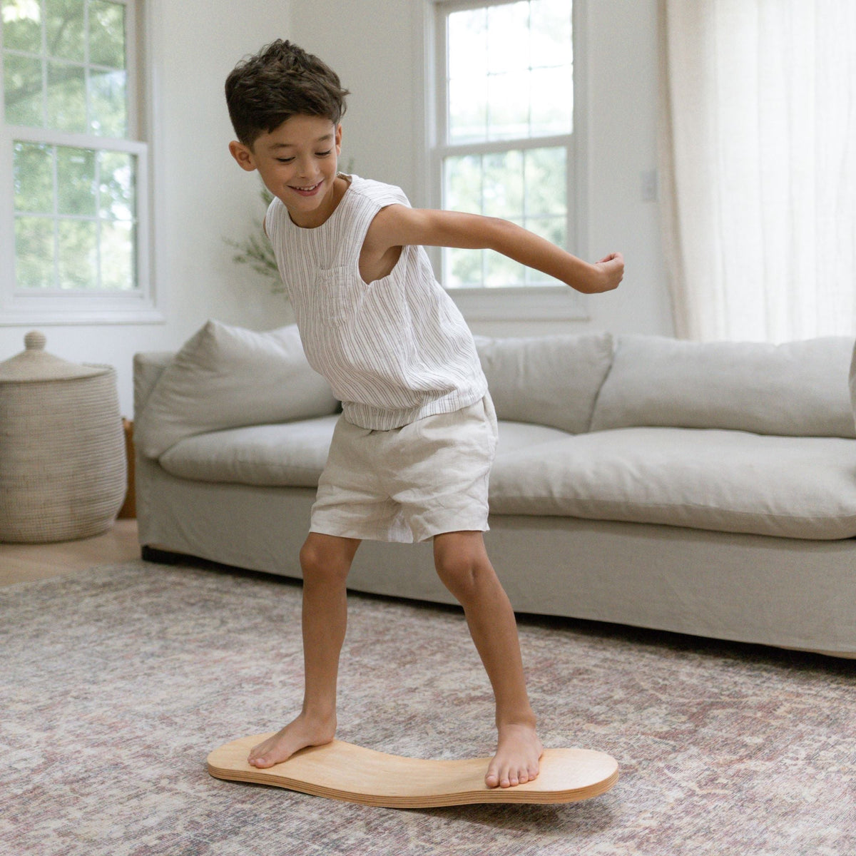 Child balancing on a pale Spinzee board with one arm extended in a living room.