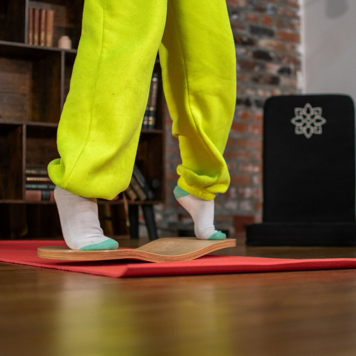 Close-up of feet in socks on a natural-tone Spinzee board placed on a red mat.