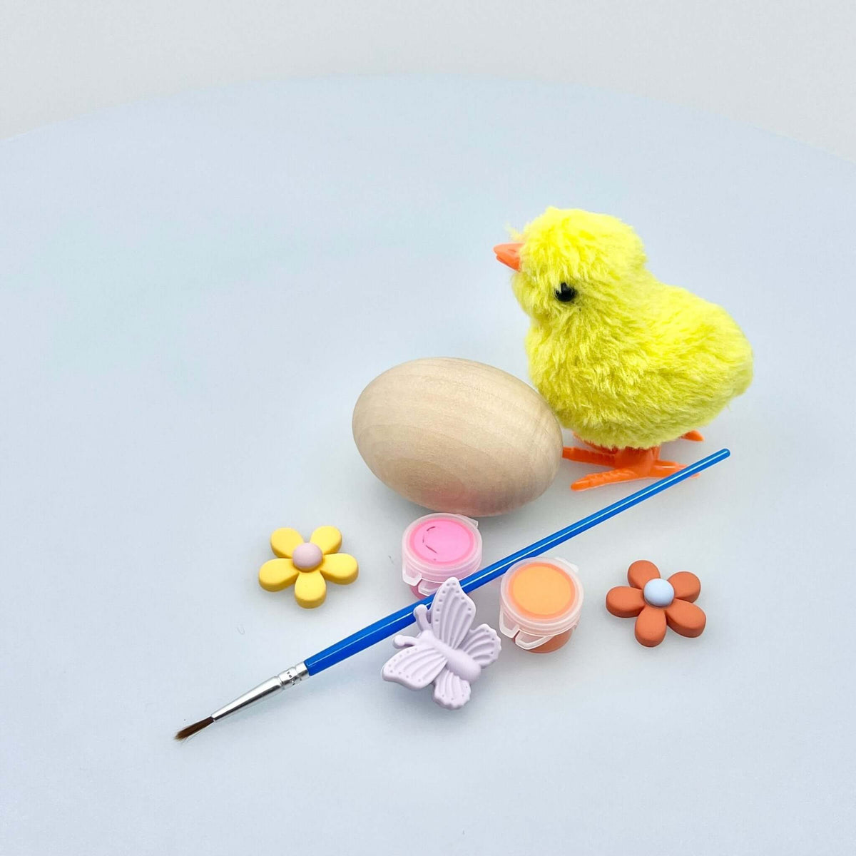 Yellow chick, unpainted egg, paintbrush, paint pots and flower and butterfly decorations