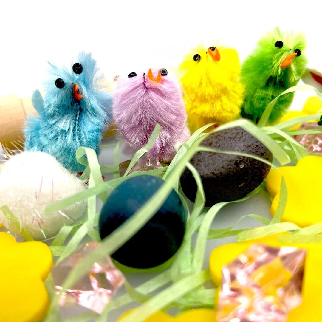 Four colorful chick figures beside two eggs and yellow playdough flowers