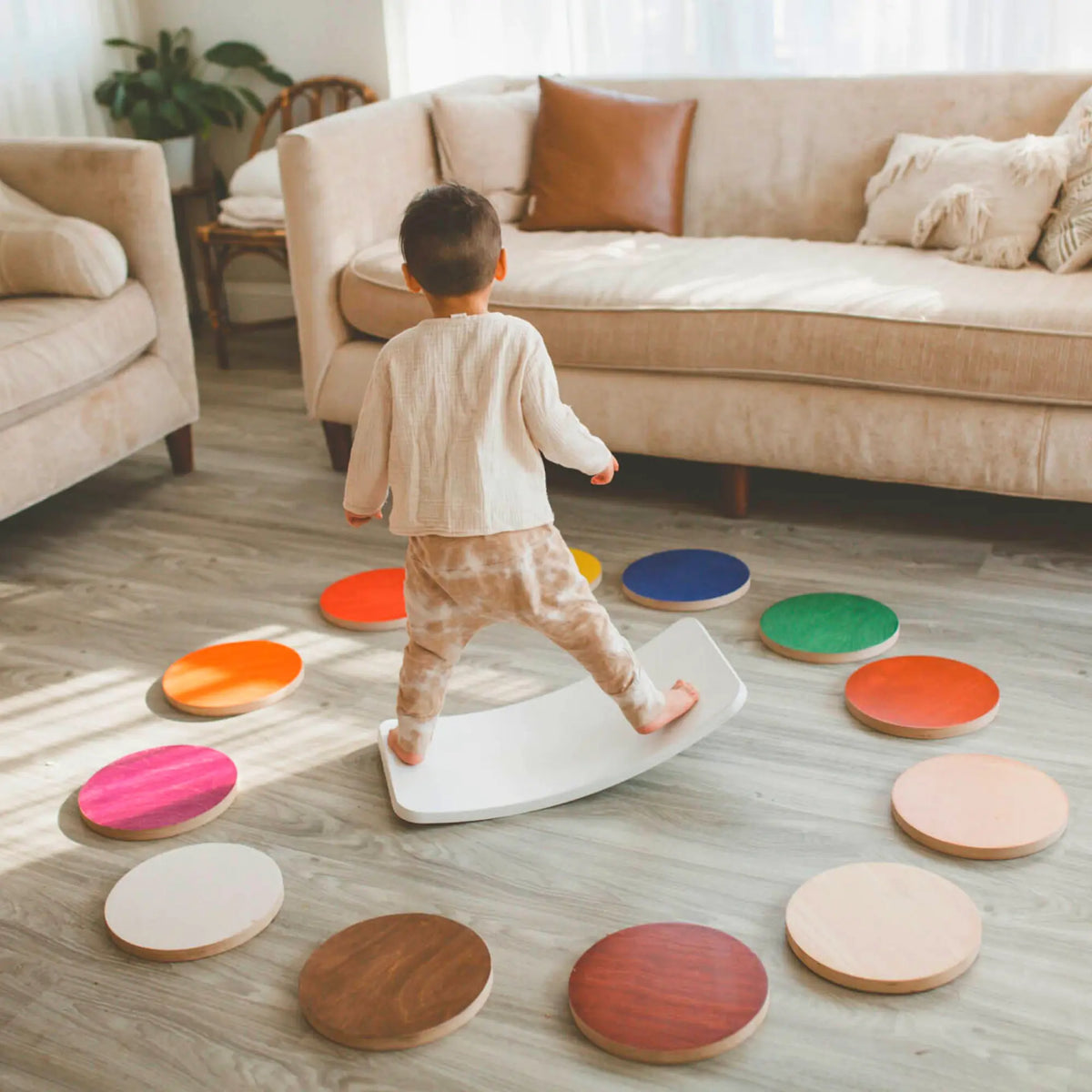 Child standing on a white wobble board surrounded by colorful and natural-tone round stepping stones.