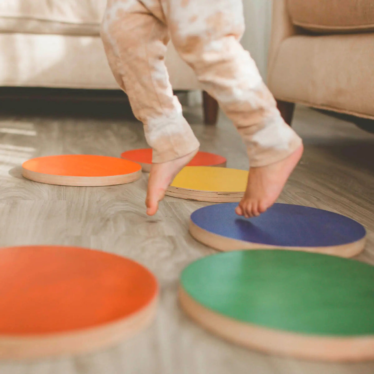 Close-up of a child stepping among orange, blue, green and yellow round stepping stones.