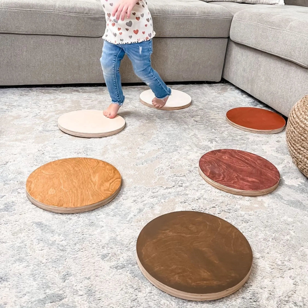 Child stepping between pale stones, with tan, brown and reddish round stones nearby on a rug.