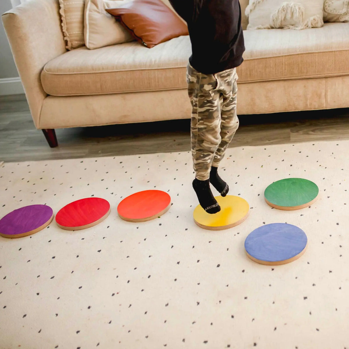 Child standing on a yellow stepping stone in a curved row of colorful round stones.