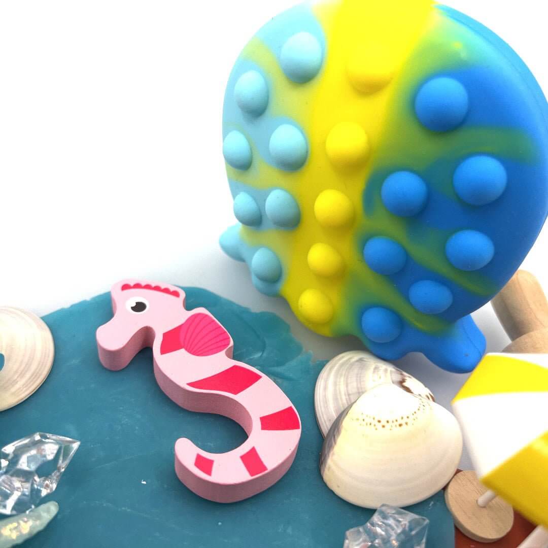 Blue-and-yellow octopus fidget beside a pink seahorse figure and shells