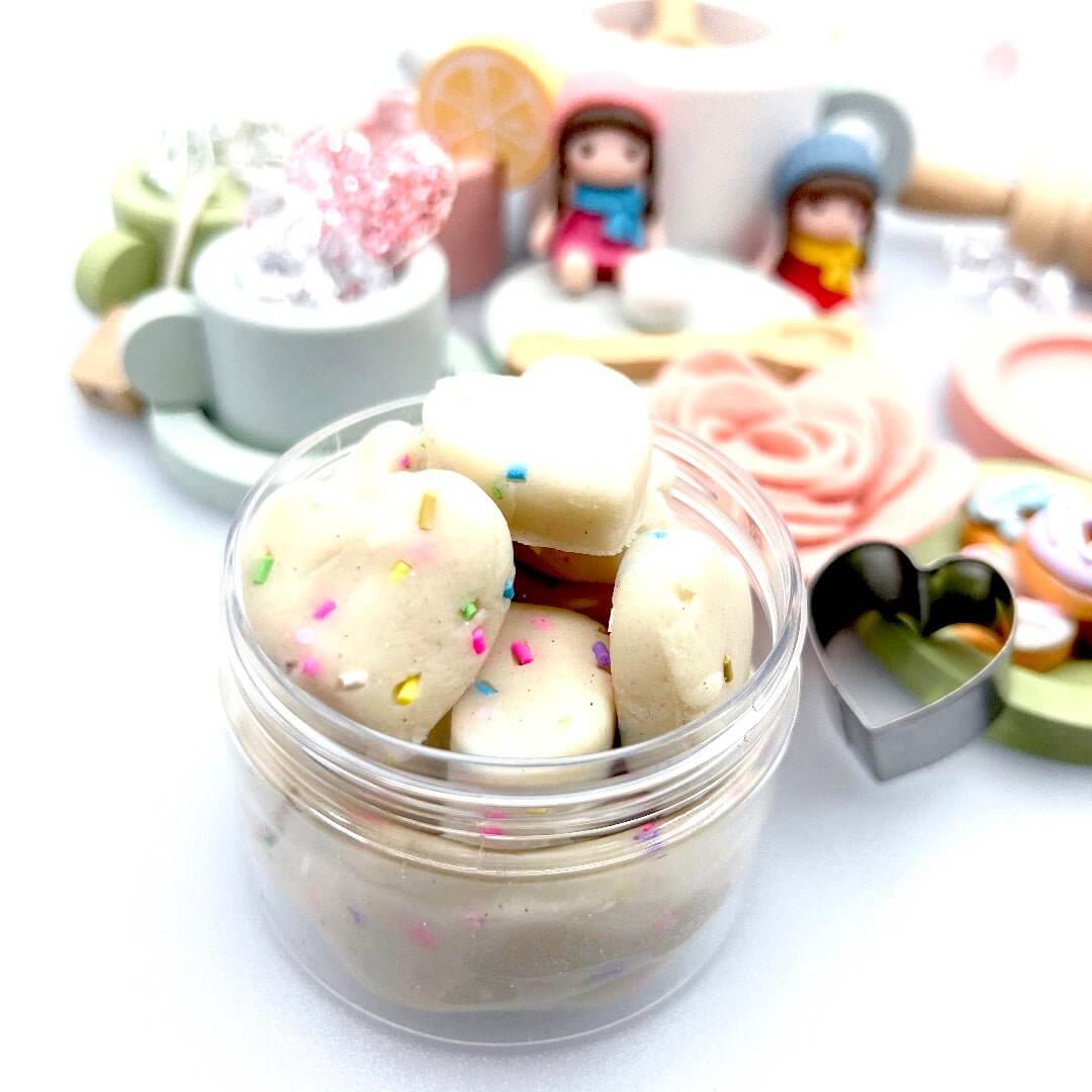 Open jar of heart-shaped playdough treats in front of the miniature tea set