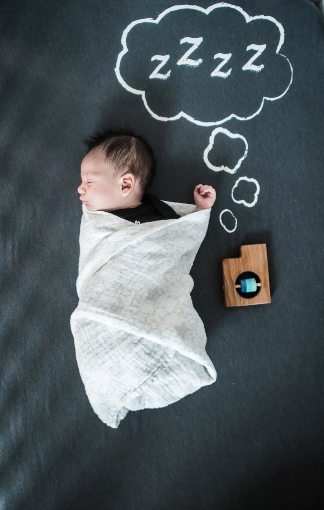 Staged nursery photo with a swaddled baby and Utah-shaped wooden rattle