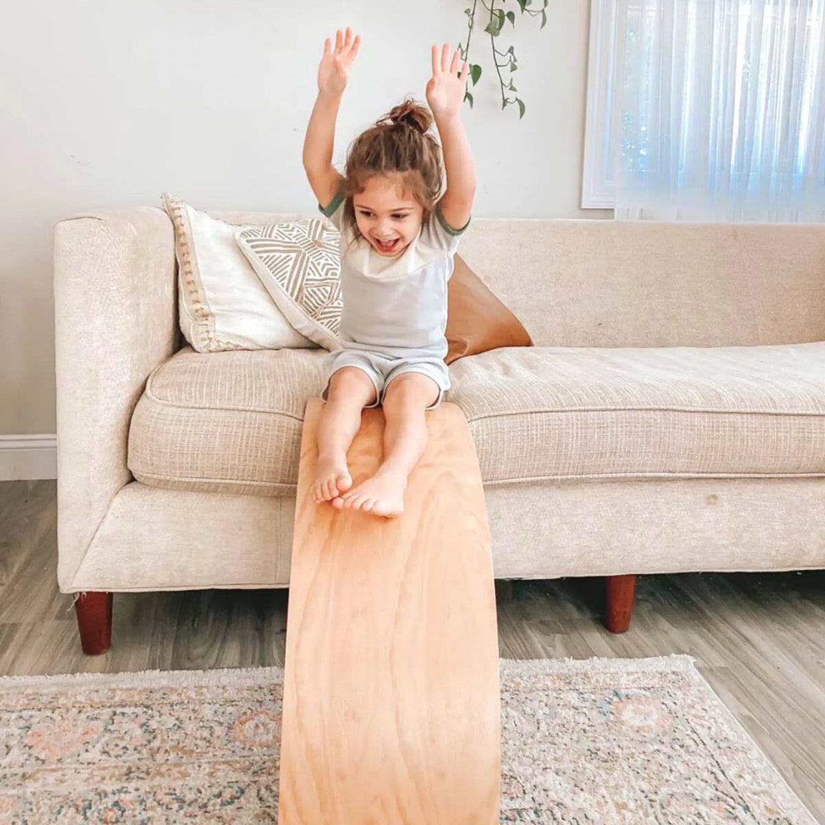 Child seated on a sofa with feet on a natural-tone wobble board positioned as a ramp.