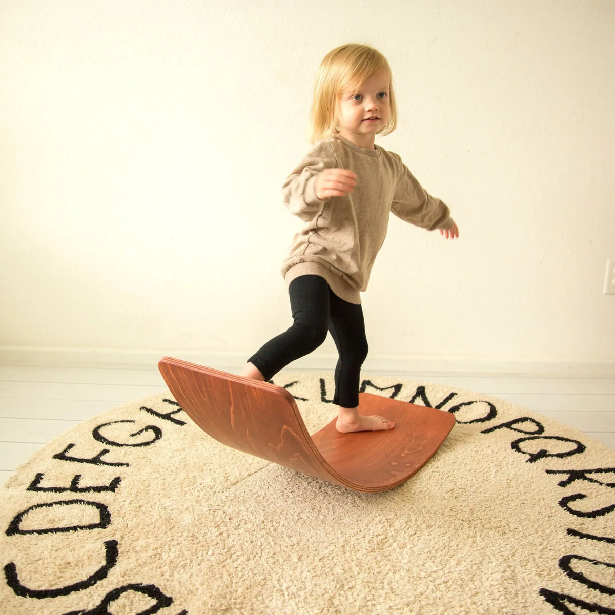 Child balancing barefoot on a reddish-brown curved wobble board.