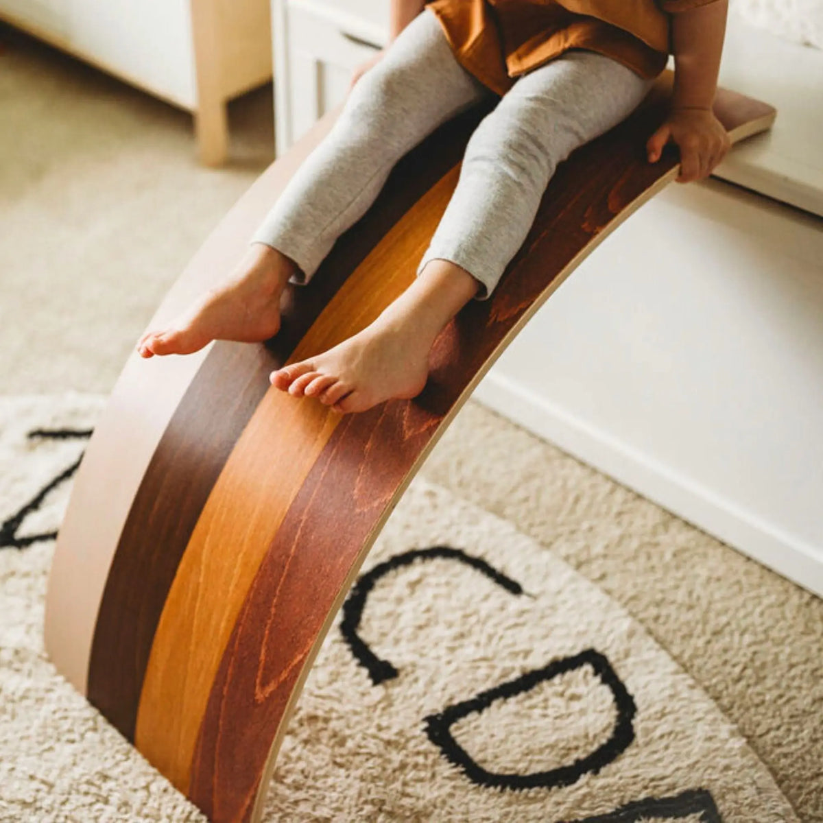 Child seated on a brown-striped wobble board propped against a window ledge as a ramp.