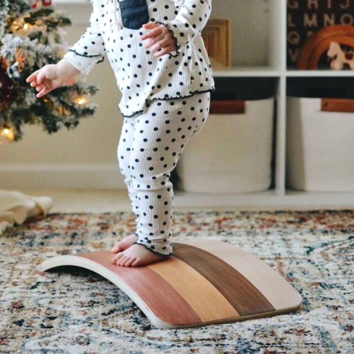 Child standing on the arch of a wobble board striped in cream, tan and brown.