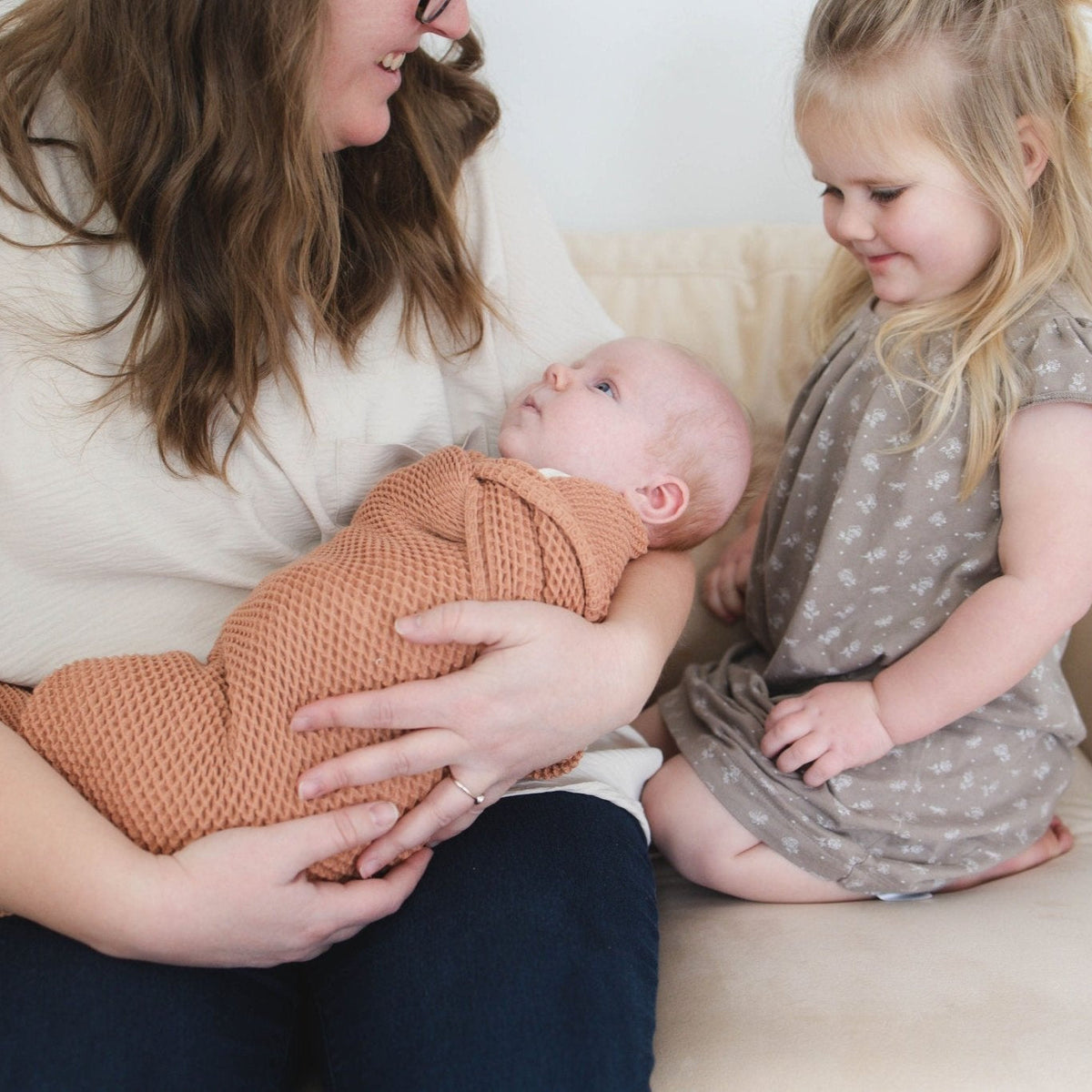 SpiritnSprout: Caregiver and older child looking at a baby in the cinnamon blanket