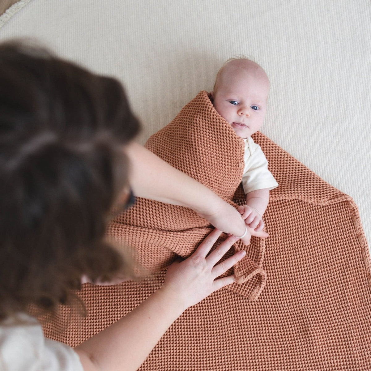 SpiritnSprout: Caregiver leaning over a baby wrapped in the cinnamon blanket
